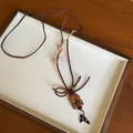 Detailed view of a cute wooden bear pendant on a brown cord necklace inside a white tray - Teddy Bear / Dark Coffee
