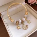 Detailaufnahme eines goldenen Stern- und Mond-Charm-Armbands mit Kristallen in einer Geschenkbox - Gold-Weiß