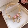 Detailaufnahme eines goldfarbenen Bettelarmbands mit Sternen, Mond und rosa Kristallperlen - Gold-Rosa