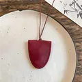 Detailopname van een handgemaakte bordeauxrode lederen brillenhouder ketting op bord. - Bordeauxrood