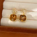 Macrodetail van vierkante gouden oorbellen met honingamberkleurige kristallen en zirkonia - Geometrisch Vierkant / Goudbruin