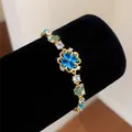 Close-up of a golden flower bracelet featuring blue heart-shaped zircon clover charms. - Four-leaf Clover Style / Gold-Blue Green Combo