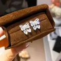 Close-up of elegant silver bow-knot stud earrings with sparkling zircons and pearls - Silver-White