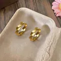 Elegant gold twisted hoop earrings with a minimalist circular design on a textured tray. - Clasp Back / Gold