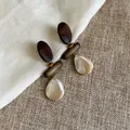 Detailansicht von Vintage-Ohrringen aus Holz und Muschelperlen auf grobem Leinenstoff - Tropfen Muschel Stil