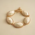 Macro view of vintage gold-toned bracelet featuring five faceted cream resin oval stones. - White