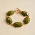 Close-up of retro gold-toned bracelet with faceted olive green oval resin stones - Green