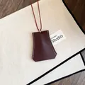 Detail van bordeauxrode lederen clochette ketting met wit stiksel en rood koordje. - Ketting / Bordeauxrood