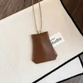Close-up van een minimalistische bruine leren sleutelhanger ketting op wit textiel. - Ketting / Bruin