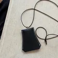 Detailaufnahme einer schwarzen Leder-Nackentasche mit weißen Nähten und Kordelzug. - Schwarz