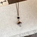 Gros plan détaillé d'un collier avec pendentif champignon marron sur un tissu beige texturé. - Forme de Champignon / Marron