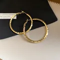 Gros plan de créoles dorées avec surface martelée élégante sur un fond texturé bicolore - Rond Plissé (Tige Argent) / Or