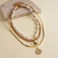 Set of 4 layered gold-tone necklaces with baroque pearls and round textured pendants. - Four-Piece Set / Gold