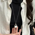 Gros plan d'un collier à pendentif ovale en argent mat sur un pull noir élégant - Argent mat