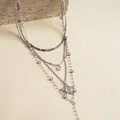 Dettaglio di una collana argentata a strati con stelle e perle su un supporto in pietra. - Collana a strati / Argento