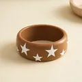Close-up van een bruine hars armband met witte sterpatronen op een beige achtergrond - Koffie met witte sterren