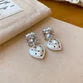 Détail rapproché de boucles d'oreilles cœur blanc avec pois noirs et cristaux brillants - Style Cœur Strass / Argent