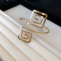 Detail view of a gold-toned geometric spiral square arm cuff on a white jewelry stand - Spiral Square Geometric Style