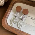 Detailweergave van handgemaakte oorbellen van hout en glas met zilveren zwaluwen. - Zwaluw Vorm / Zilveren Oorknopje Stijl / Zilver Bruin