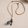 Détail d'un collier ethnique en cuir avec fleur en céramique bleue et perles de bois - Café-Bleu