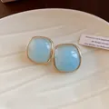 Close-up of light blue resin square stud earrings with gold border on a white plate - Silver Earring Post-Blue