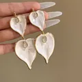 Macro view of vintage gold earrings featuring elegant white heart-shaped enamel droplets - Double Layer Heart Dangle Style / Gold with White