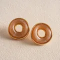 Makroaufnahme der bernsteinfarbenen Vintage-Ohrstecker aus Acryl mit Goldrand. - Orange