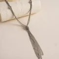 Makroansicht einer mehrlagigen Metallkette mit elegantem Quastenknoten und kleinen Perlen - Silber