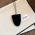 Close-up of a black shield-shaped leather necklace pendant and glasses holder on canvas. - Black