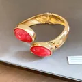 Close-up of elegant gold open bangle with vibrant red oval resin stones and hinged design. - Gold Red