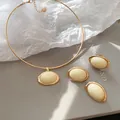 Detailansicht eines goldenen Schmucksets mit ovalen cremefarbenen Harzsteinen auf grau. - Ohrringe Ring Choker / Gold-Weiß
