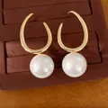 Close-up of geometric gold earrings with large white pearls on a velvet tray - Gold, White