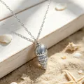 Macro view of a stainless steel conch shell pendant on a sunny beach setting - Steel