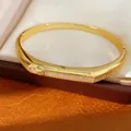 Close-up of 18K gold plated bangle featuring sparkling zircon stones and oval buckle design. - Gold