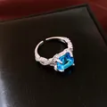 Close-up of luxury silver-toned open ring featuring a square blue zircon and pavé accents. - Ring-Silver-Blue
