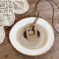 Dettaglio di collana in stile etnico con pendente in legno scuro e corda beige avvolta - Telaio in Legno con Corda Intrecciata Beige / Marrone