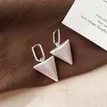 Detailopname van elegante zilverkleurige driehoekige hangoorbellen op bruine achtergrond - Mat Zilver