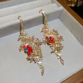 Detailansicht luxuriöser Zirkon- und Glasblumen-Quasten-Ohrringe in einer Schmuckschachtel. - Ohrhaken-Stil / Gold-Rot