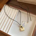 Macro view of minimalist matte gold pendant on black cord necklace inside wooden jewelry box - Matte Gold