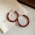 Detailansicht von burgunderroten Emaille-Creolen mit weißen Punkten auf Geschenkbeutel - Silberner Ohrring-Stift - Rot