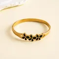 Gros plan d'un jonc en acier inoxydable doré orné de fleurs en émail noir fin - Bracelet jonc / Or-Noir