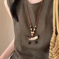 Close-up van een boho houten kralenketting met een bloemenhanger op linnen kledingstuk - Koffie-Roze-Paars