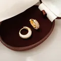 Nahaufnahme eleganter zweifarbiger geometrischer Creolen in Gold und Weiß mit Kristallen - Gold