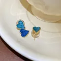 Elegant asymmetrical blue heart earrings with drip oil finish on a ceramic dish - Gold Blue Ear Clips