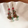 Close-up of vintage bronze flower earrings with red and green beads in a white bowl. - Ethnic Style Floral Tassel (31#) / Hook Style / Copper-Red-Green