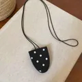 Nahaufnahme einer schwarzen Lederbeutelkette mit weißen Punkten auf beigem Hintergrund - Schwarzer Polka Dot