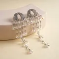 Detailopname van elegante zilveren kwastjesoorbellen met fonkelende strassteentjes en glaskralen - Zilver