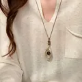 Dichtbij van een vintage tijgeroog hanger ketting gedragen op een crème v-hals trui - Ketting / Licht Koffiegoud
