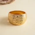 Detailweergave van gouden brede armband met unieke geplooide metaaltextuur. - Goud