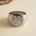 Close-up van een zilveren metalen manchetarmband met een kenmerkende gerimpelde golftextuur. - Zilver